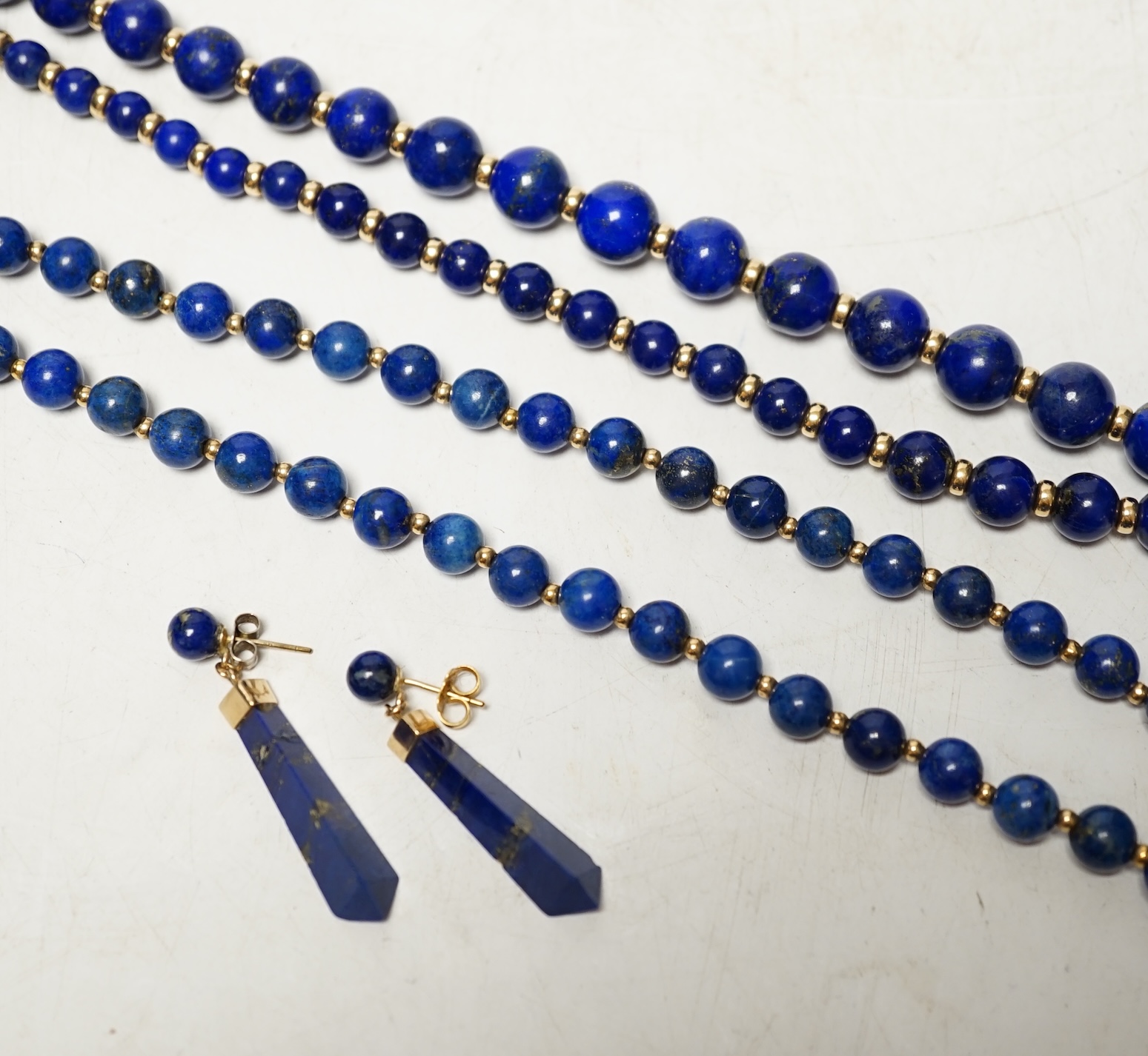 Two lapis lazuli bead necklaces with yellow metal spacers, largest 76cm and a pair of earrings. Condition - fair